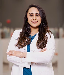 Dr. Johal, Dentist in white lab coat and teal scrubs, arms crossed and smiling in clinic reception area